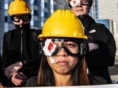 Demonstrators stand at a vigil with yellow helmets, goggles, and symbolically covered right eyes in front of the Chinese Embassy and demand freedom for Hong Kong.