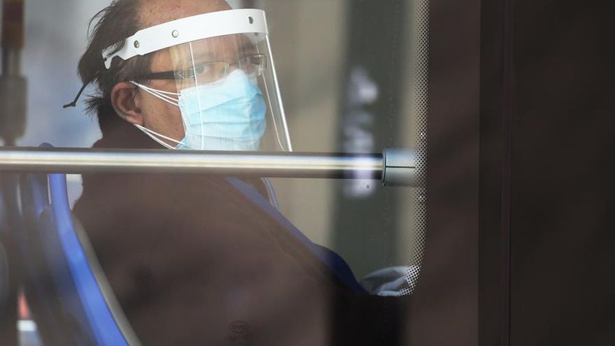 Un hombre usa tapabocas y protector facial mientras se transporta en bus